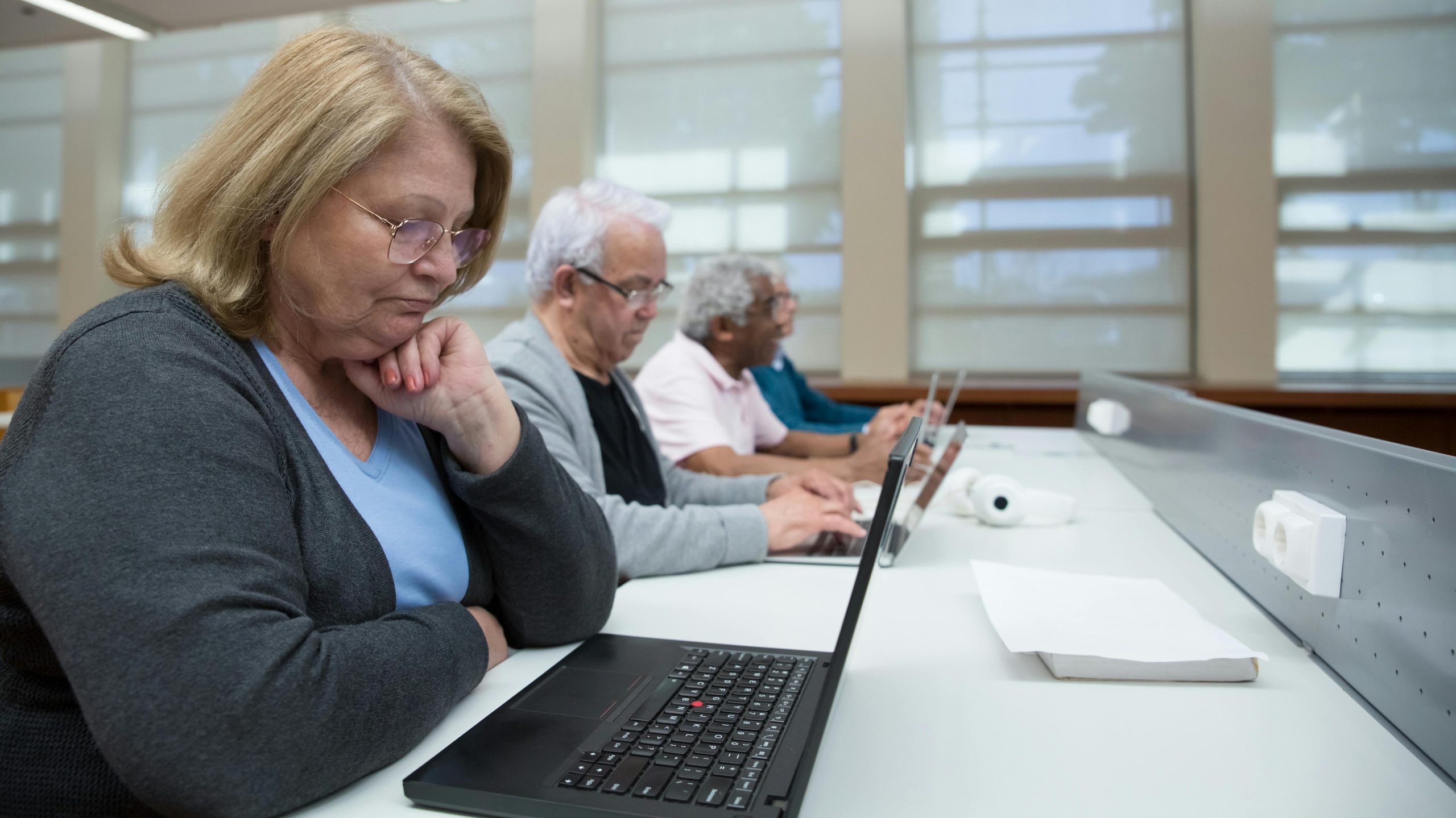 pranayama Seniors engaged in a computer class, learning digital skills with laptops indoors.